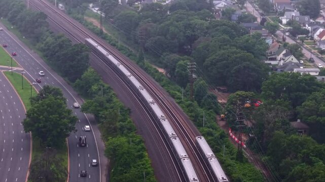 An aerial view of two Long Island Rail Road trains traveling on a cloudy day. The drone camera tilted downward, dolly in and tilt up to follow the trains moving towards New York City.