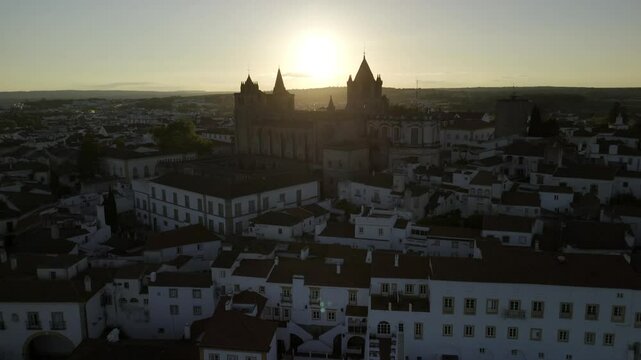 Drone flies into the sunset low over neighborhood and roof of cathedral in Evora, Portugal