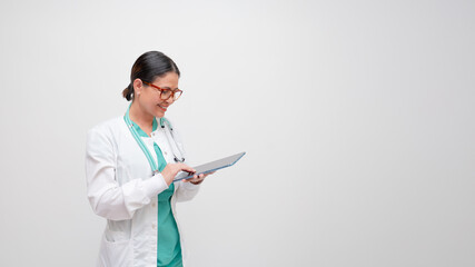 Happy doctor smiling as she looks down interacts with electronic device with white lab coat and...