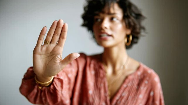 Woman hand stop gesture warning serious jewelry ring earring gold, short curly brown hair, rust blouse, fashion indoor, confident adult female expressing refusal and assertiveness with selective