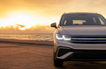 Silhouetted by a colorful sunset, a gray car stands near the ocean's edge. The warm light and open space capture a moment of solitude and exploration. 