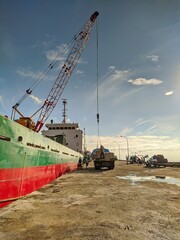 Cargo ship undergoes loading and unloading along a concrete quay on a bright, sunny day