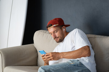 Man scrolling social media on smartphone on sofa at home near surfboard.