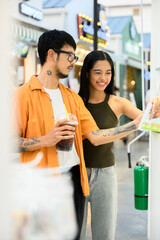 Young couple exploring street market, enjoying refreshing drinks in Bangkok