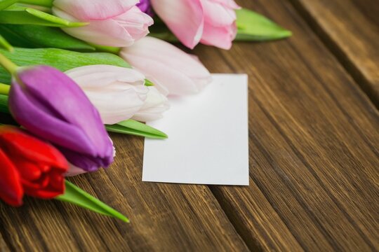 Fototapeta Cluster of multicolored tulips and blank white card is being shown on wood tabletop, flat design