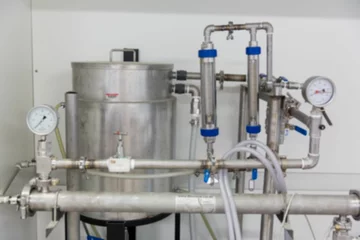 Stainless steel unit is showing flat design with tank, pipes, valves, gauges against plain wall
