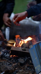 small fire on a pile of wood with several human hands are seen preparing adding fuel to the fire,...