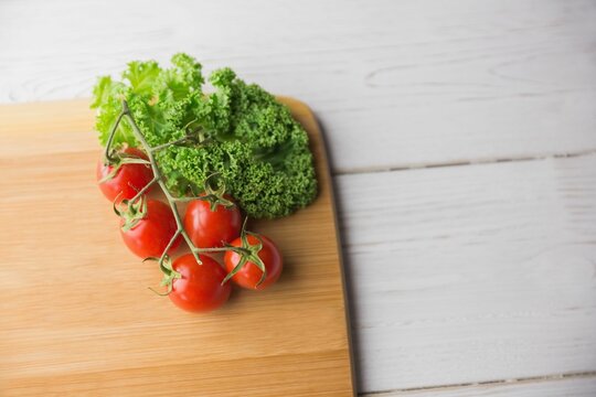 Fototapeta Tomatoes and parsley on chopping board over wooden floor