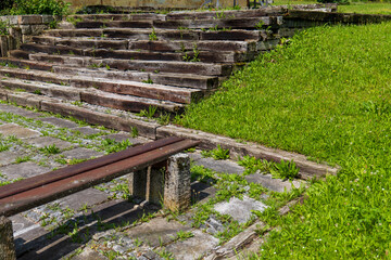 Old weathered wooden steps overgrown with weeds. Abandoned outdoor seating or amphitheater in a state of natural decay.