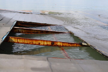 Rusted metal beams on a damaged floating platform offshore, structural parts partially hidden...