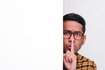 Adult Asian man face peeking behind wall doing silent hand gesture