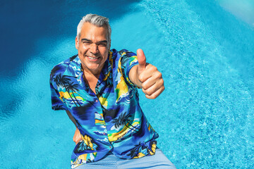 Happy mature tourist giving thumbs up by the poolside