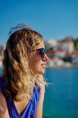 Side view of woman in sunglasses and blue dress looking at the sea on sunny day. Female tourist...