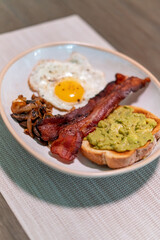 Hearty breakfast plate with crispy bacon, fried egg, sautéed mushrooms, and creamy avocado toast on rustic ceramic dish—perfect for brunch menus, food blogs, or nutrition features.