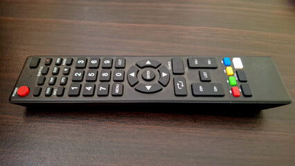 Angled side view of a black TV remote control resting on a dark wood surface. The image highlights...