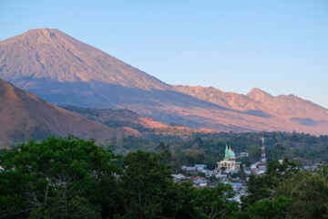 Breathtaking morning panorama of Mount Rinjani from Bukit Selong, Sembalun—sunlight softly...