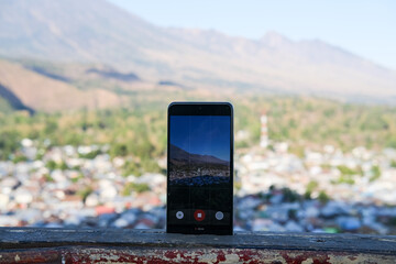 Smartphone captures scenic mountain view of Lombok from rooftop, blending modern technology with breathtaking natural beauty.