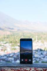 Smartphone captures scenic mountain view of Lombok from rooftop, blending modern technology with breathtaking natural beauty.