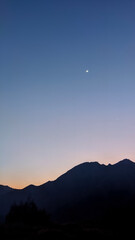 Glowing twilight sky blankets the rolling hills of Sembalun, Lombok, painting the horizon in soft purples and oranges as mountain silhouettes fade into serene dusk.