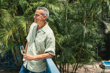 Mature man enjoying a glass of champagne on a tropical balcony