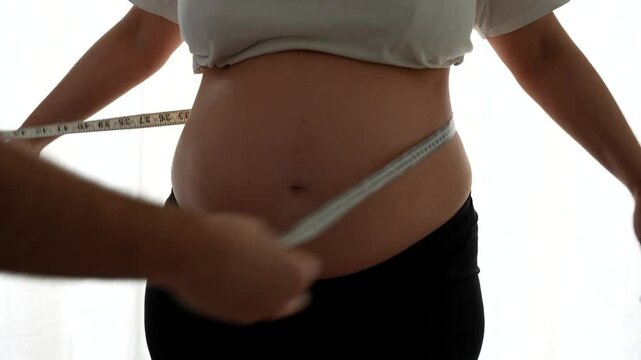 Man measuring with a tape measure his pregnant wife's belly