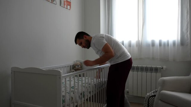 Young father putting up baby crib bedding sheets at home