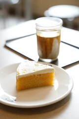 Cup of milk dirty coffee with a piece of lemon cake on table by the window.