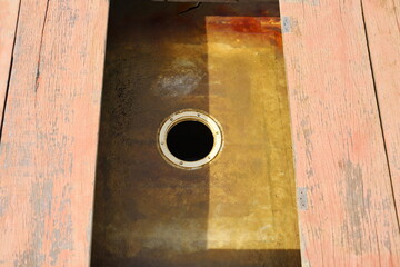 Close-up view of a circular access hole in a rusty metal surface, surrounded by aged pink-painted...