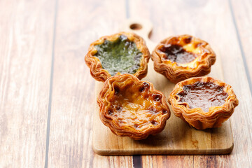 Stack of assorted Portuguese sweet dessert egg tart or Pastel de Nata on wooden board on wooden table.
