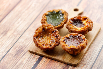 Stack of assorted Portuguese sweet dessert egg tart or Pastel de Nata on wooden board on wooden table.