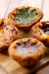 Stack of assorted Portuguese sweet dessert egg tart or Pastel de Nata on wooden board on wooden table.