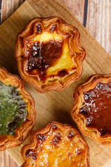 Stack of assorted Portuguese sweet dessert egg tart or Pastel de Nata on wooden board on wooden table.
