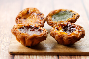 Stack of assorted Portuguese sweet dessert egg tart or Pastel de Nata on wooden board on wooden table.