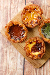 Stack of assorted Portuguese sweet dessert egg tart or Pastel de Nata on wooden board on wooden table.