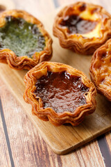 Stack of assorted Portuguese sweet dessert egg tart or Pastel de Nata on wooden board on wooden table.