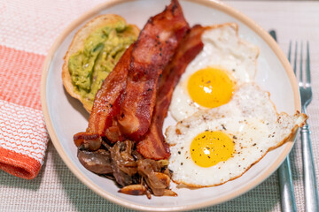Hearty breakfast plate with crispy bacon, fried egg, sautéed mushrooms, and creamy avocado toast on rustic ceramic dish—perfect for brunch menus, food blogs, or nutrition features.