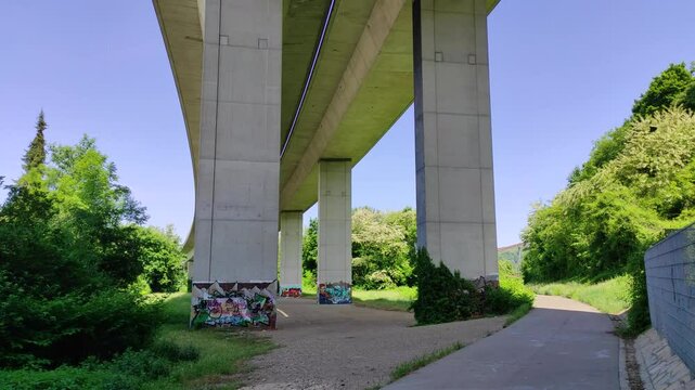 Underneath a highway with pillars, trees, bike path, tilt-up shot