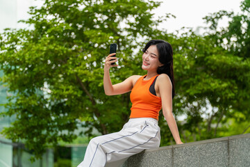 Young Asian woman having a video call on phone in green city park