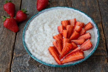 Oatmeal porridge with fresh strawberries in a plate on a wooden table