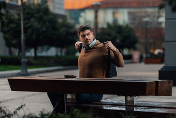 Businessman putting on backpack while sitting on bench outdoors