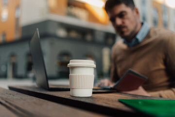 Businessman working outdoors with reusable coffee cup and laptop