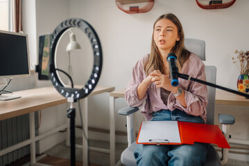 Young woman recording podcast in home studio using ring light and microphone