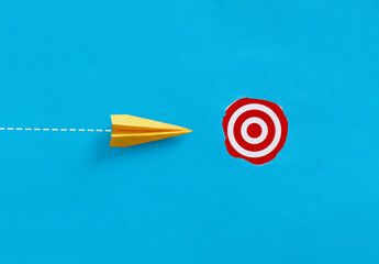 Yellow paper airplane flying towards red target on blue background