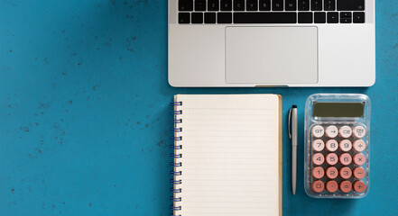 Laptop, notebook, pen and calculator forming a workspace on blue desk