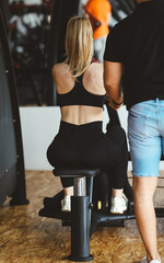 Woman training on a rowing machine with personal trainer guidance at a modern gym, focusing on...