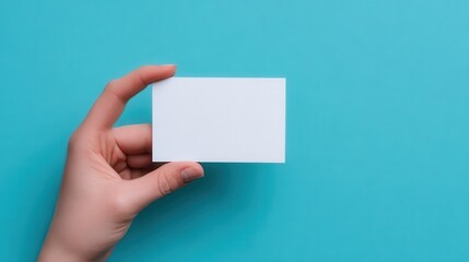 Fototapeta premium A hand holds a blank white business card against a solid teal background.