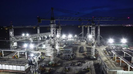 Massive construction site illuminated by bright floodlights at night with multiple tower cranes in action, representing industrial development, engineering, and modern infrastructure growth