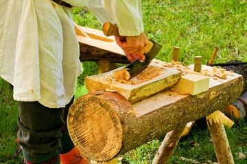 Traditional Woodworking Craftsman Using Axe and Adze. Man in Historical Costume Carving Wooden Log.