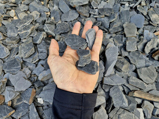 man holds in his hand a sample of stone gravel or pebbles of one size. Marble white gravel and gray brown pebbles straight from the quarry. sample