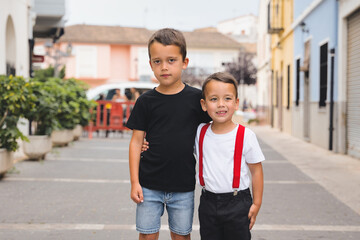 Two young brothers embracing on a lively town street, wearing casual clothes and sharing joyful...